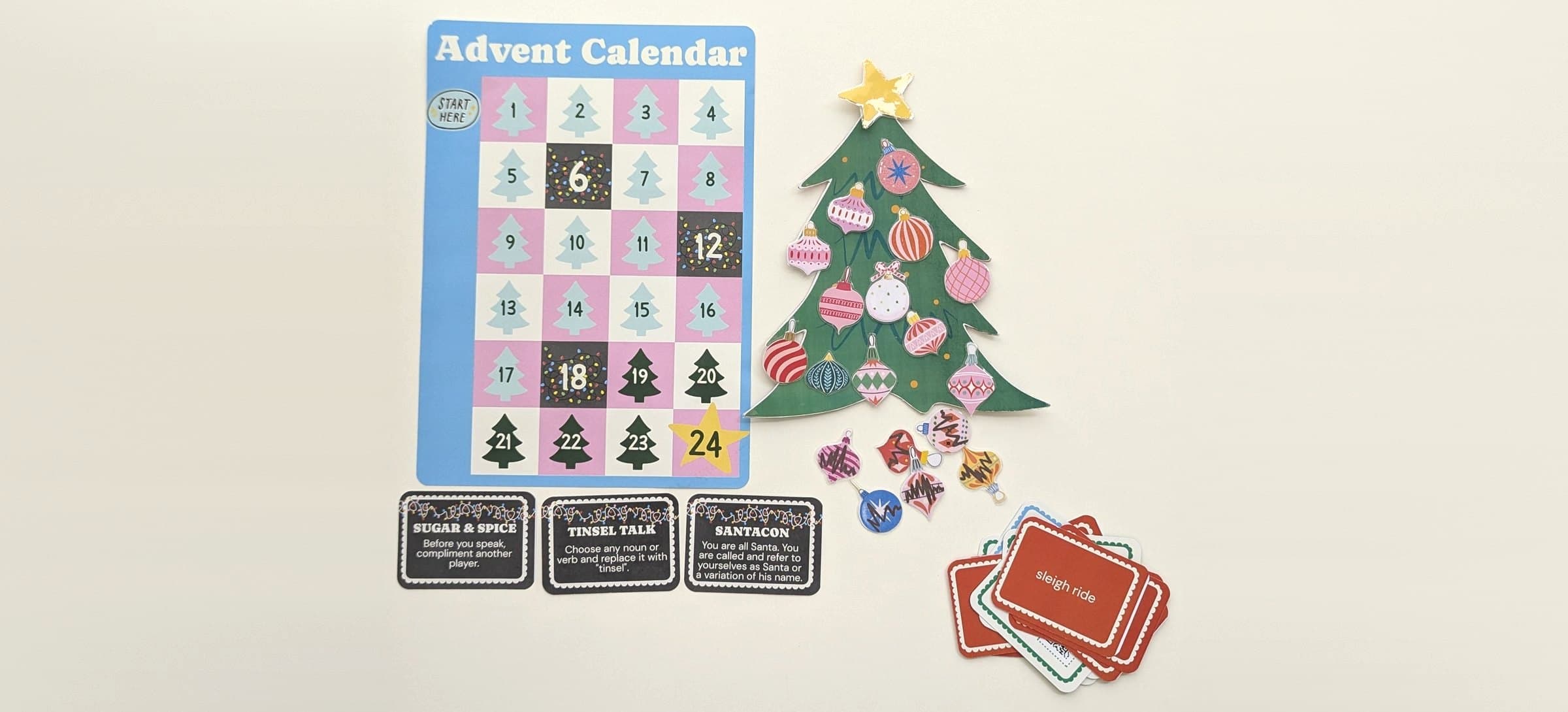 Der Adventskalender, ein geschmückter Weihnachtsbaum, drei Chaos-Karten und ein Stapel Truth-, Carol- und Challenge-Karten auf einem Tisch